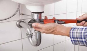 Hands use a wrench to fix a pipe on a bathroom sink.